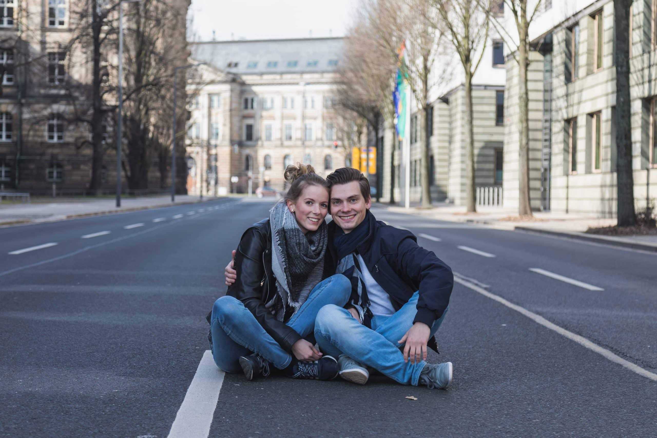 ein Paar hat sich in den Arm und sitzt auf einer Straße eng beieinander und schauen in die Kamera