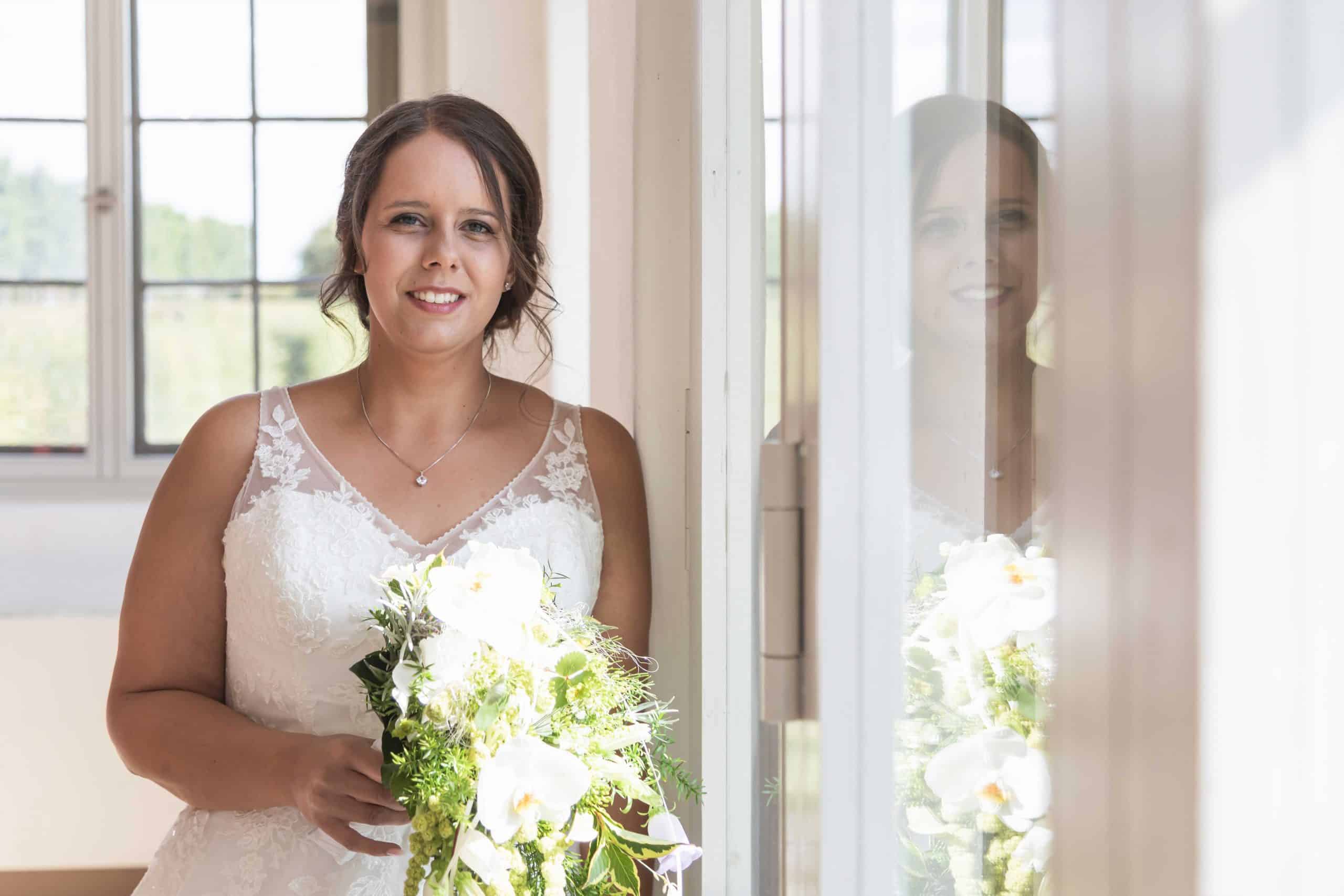 Frau im Brautkleid lächelt in die Kamera, während sie einen Blumenstrauß hält.