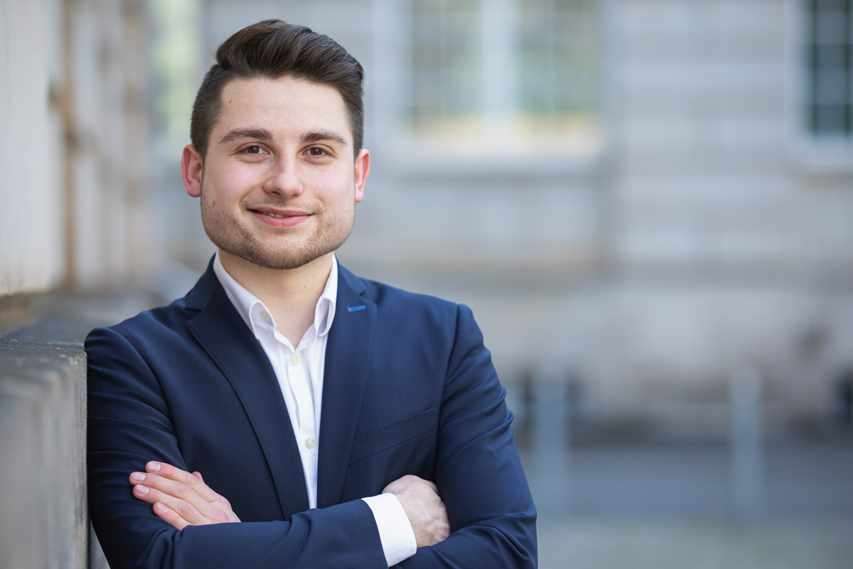 Jan Windisch, Fotograf und Hochzeitsfotograf aus Dresden, Prina, Görlitz, Großenhain und Leipzig, hat hier ein Mann fotografiert. Er steht frontal zur Kamera und lehnt mit der rechten Schulter an der Wand. Er schaut in die Kamera und lächelt.