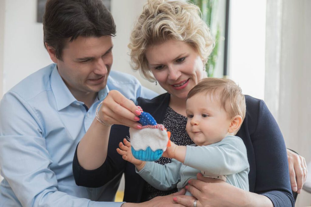 Jan Windisch, Fotograf und Hochzeitsfotograf aus Dresden, Prina, Görlitz, Großenhain und Leipzig, hat hier eine Familie mit einem Kind fotografiert. Die Eltern sitzen frontal zur Kamera und die Mutter hat das Kind auf dem Schoß. Das Kind schaut Richtung Kamera und hält ein Spielzeug in der Hand.