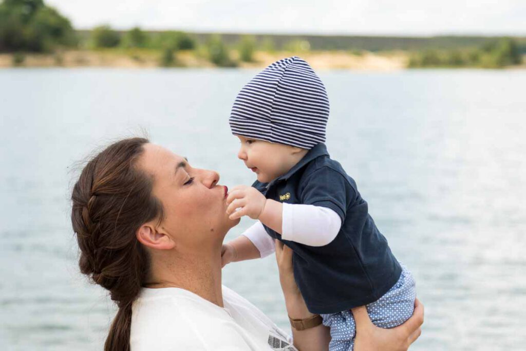 Jan Windisch, Fotograf und Hochzeitsfotograf aus Dresden, Prina, Görlitz, Großenhain und Leipzig, hat hier eine Mutter mit ihrem Kind fotografiert. Beide werden von der Seite dargestellt und die Mutter hat ihr Kind mit beiden Händen hochgehoben und will ihm ein Kuss geben.