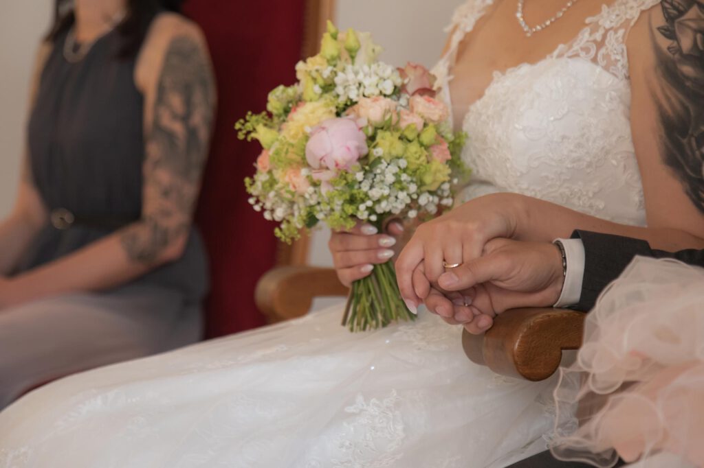 während der standesamtlichen Zeremonie halten sich das Brautpaar die Hände.