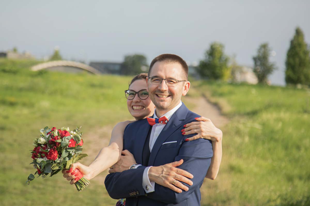Jan Windisch, Fotograf und Hochzeitsfotograf aus Dresden, Prina, Görlitz, Großenhain und Leipzig, hat hier ein Brautpaar fotografiert. Sie steht hinter dem Bräutigam und hat einen Arm um seine Schultern geschlungen. In der anderen Hand hält sie einen Blumenstrauß.