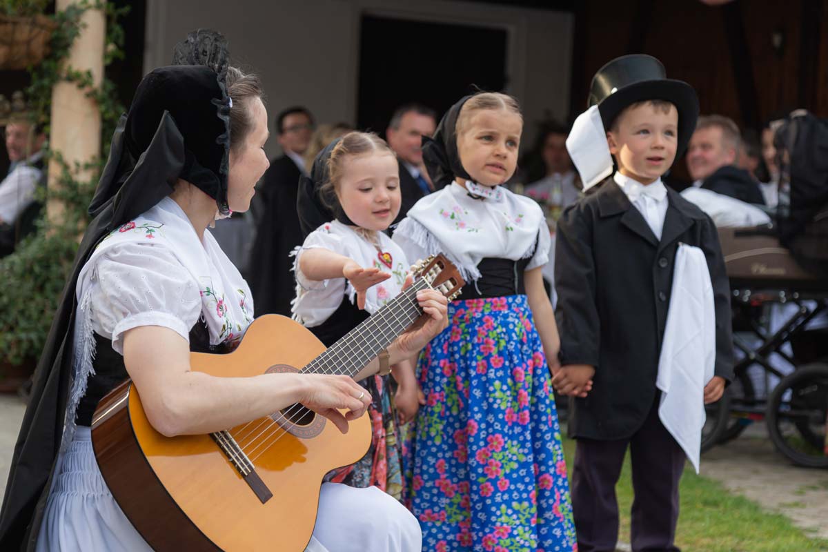 Bei einer traditionellen sorbischen Hochzeit singen Kinder und eine Frau spielt dabei Gitarre. Alle haben viel Spaß.