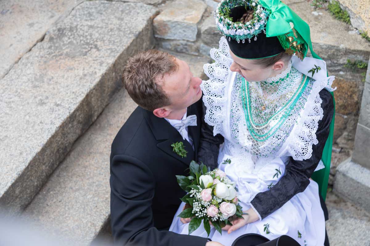 Jan Windisch, Fotograf und Hochzeitsfotograf aus Dresden, Bautzen, Prina, Görlitz, Großenhain und Leipzig, hat hier ein sorbisches Brautpaar fotografiert. Die Frau sitzt bei dem Bräutigam auf dem Schoss und schauen sich verliebt in die Augen.