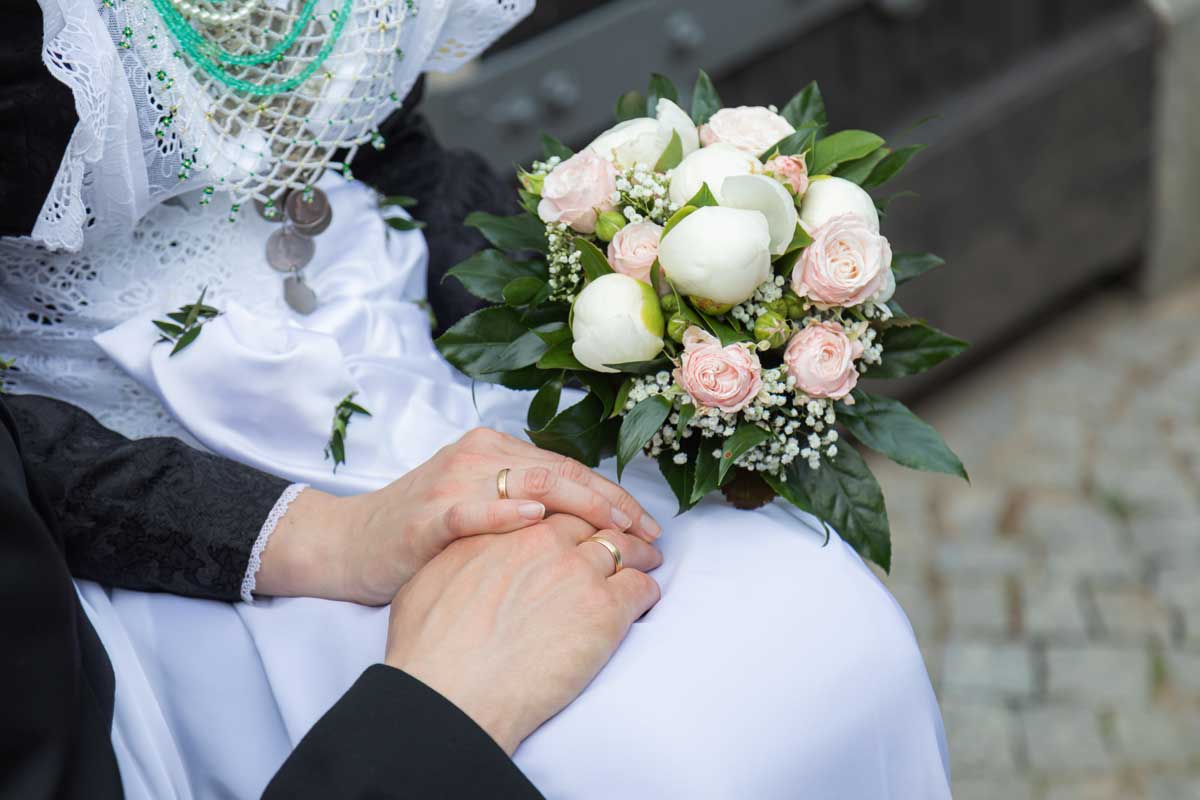 Das Ehepaar hält sich an den Händen und die Braut hält zusätzlich noch den Brautstrauß fest.