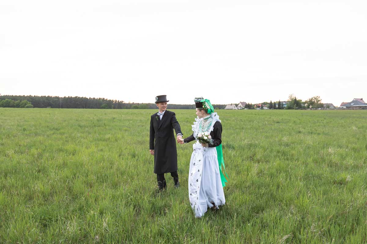 Jan Windisch, Fotograf und Hochzeitsfotograf aus Dresden, Prina, Görlitz, Großenhain und Leipzig, hat hier ein sorbisches Brautpaar fotografiert. Beide laufen über eine Wiese mit der typischen Tracht.