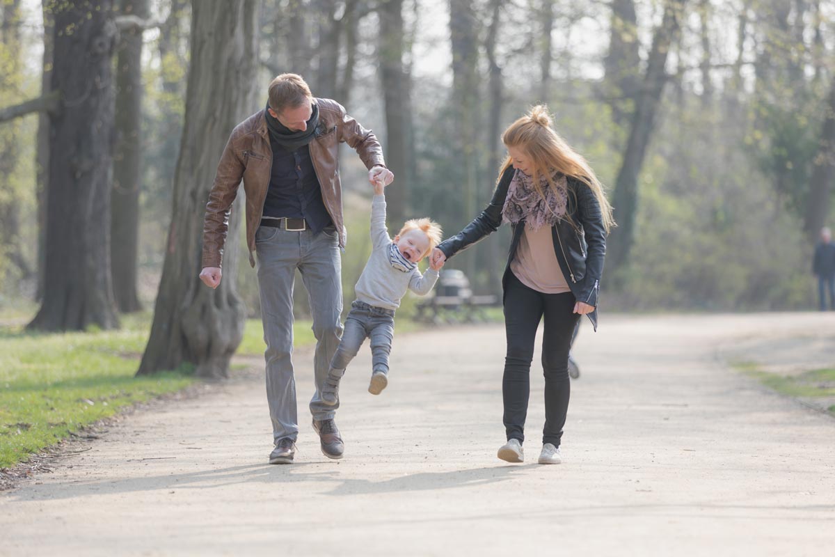 eine junge Familie gehen spazieren und dabei hat der Sohn viel Spaß. Die Eltern ziehen ihn hoch und springen so mit ihm vorwärts.