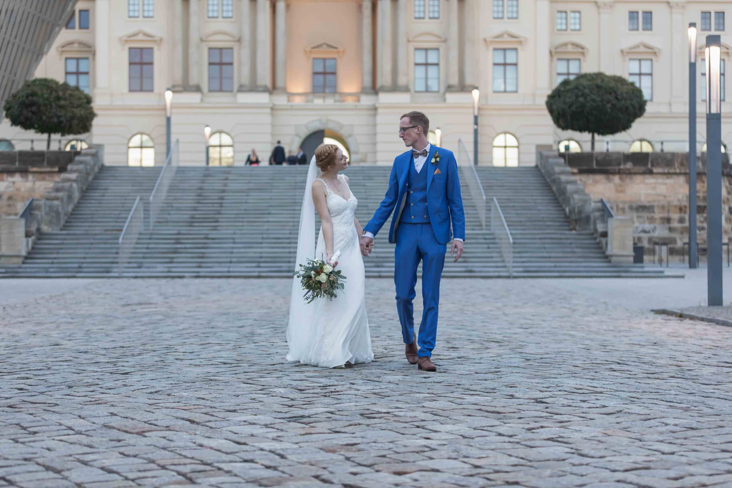 Hochzeitsfotografie in Freiberg - professionelle Fotos einer Hochzeit und seinem Brautpaar. Das Brautpaar geht eine Straße entlang, sie halten sich an den Händen fest und schauen sich verliebt an. Dabei genießen sie den wohl schönsten Tag - ihren Hochzeitstag!